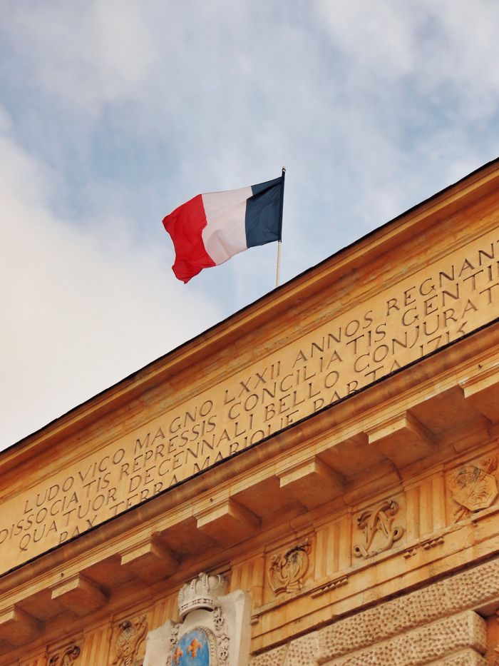 Low angle view of the French flag waving atop a historic building in Montpellier, France.