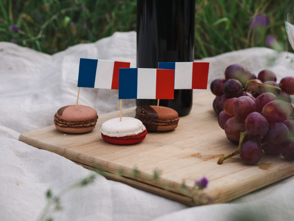 Macarons decorated with French flags on a picnic setup with grapes and wine.